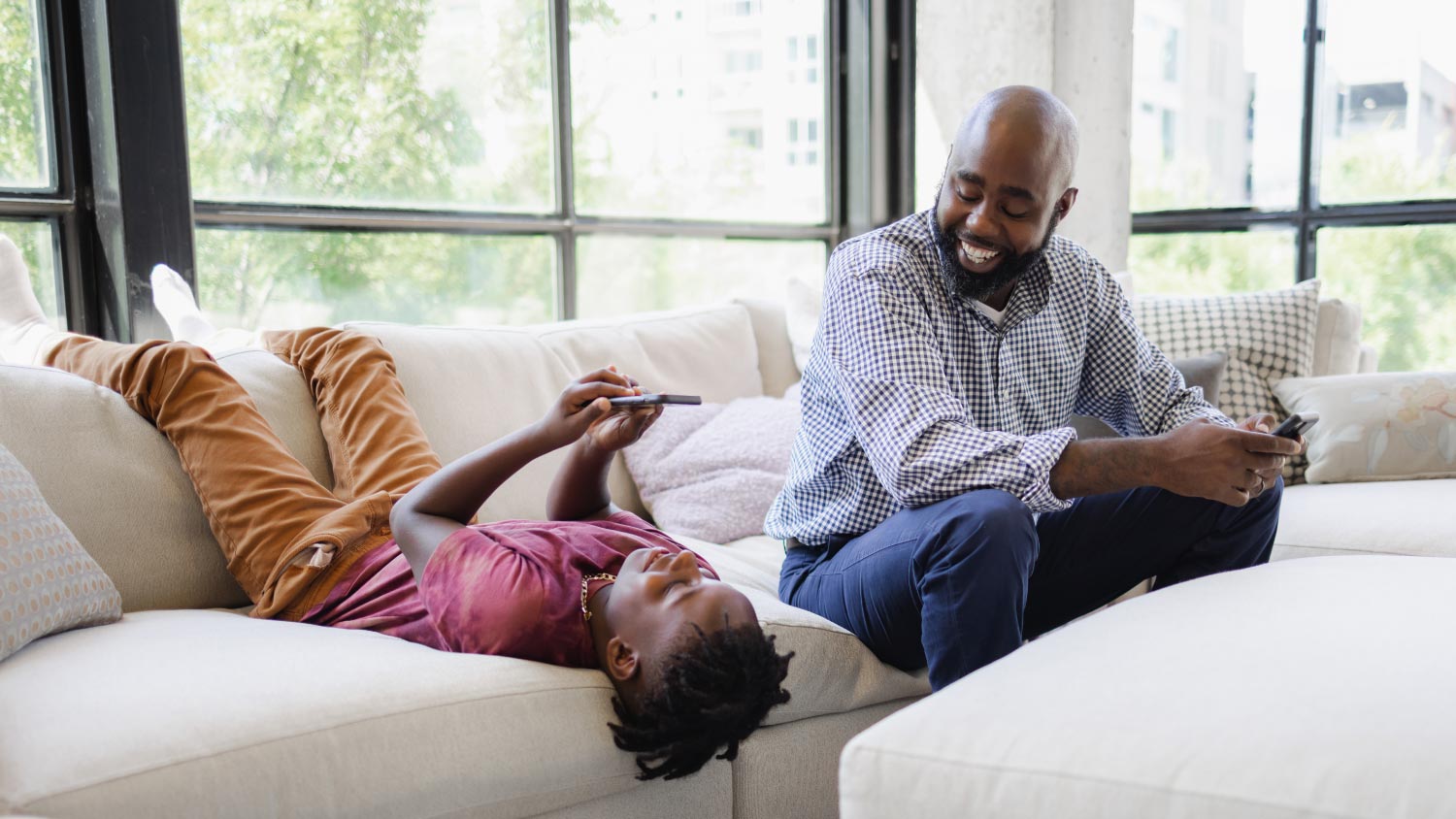 Father and son using smartphones on sofa
