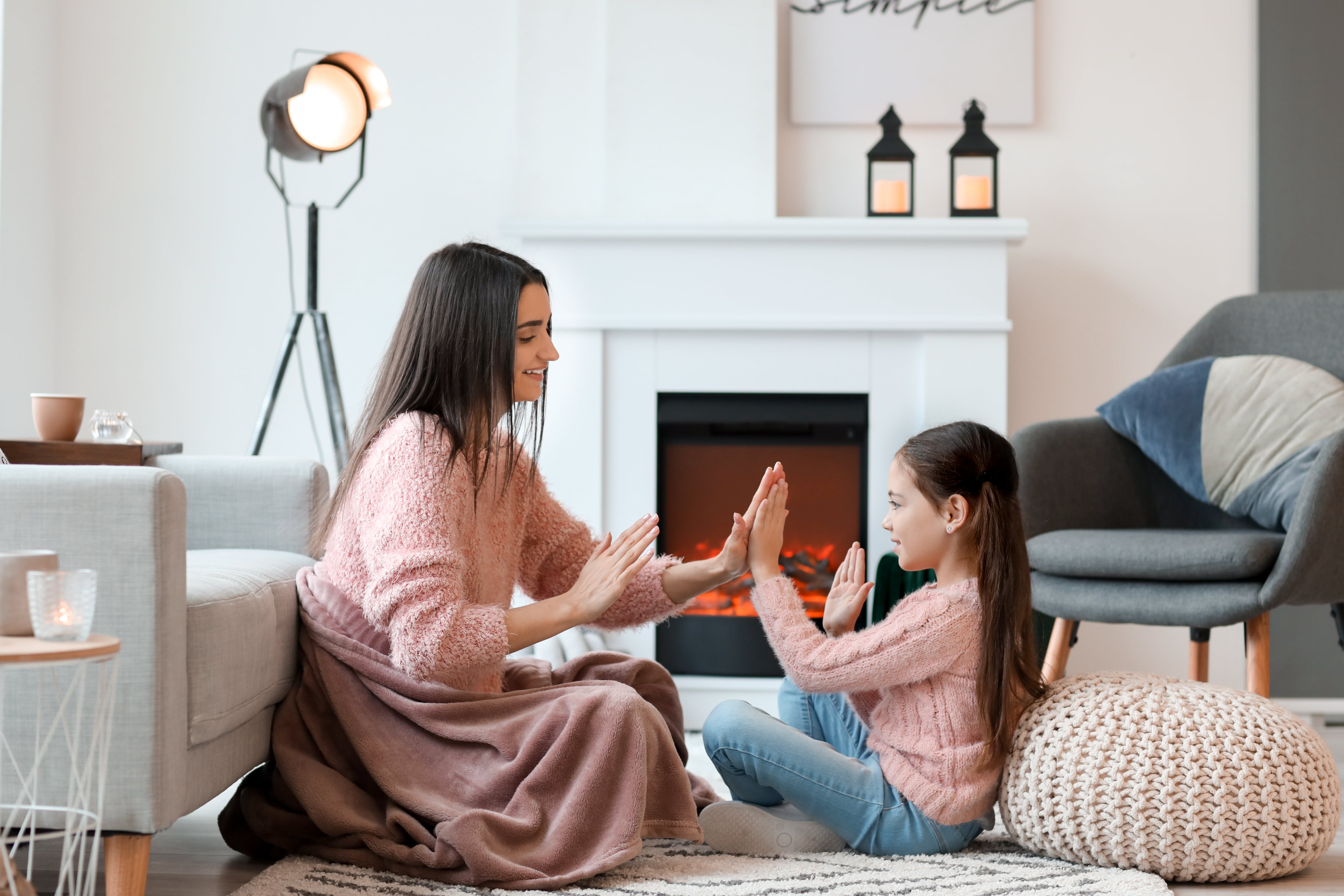 Mother and daughter sitting and playing clapping games in front of a fireplace 