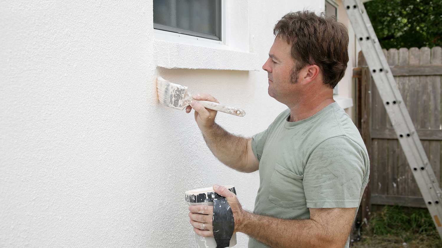 Handyman painting stucco exterior wall with a brush