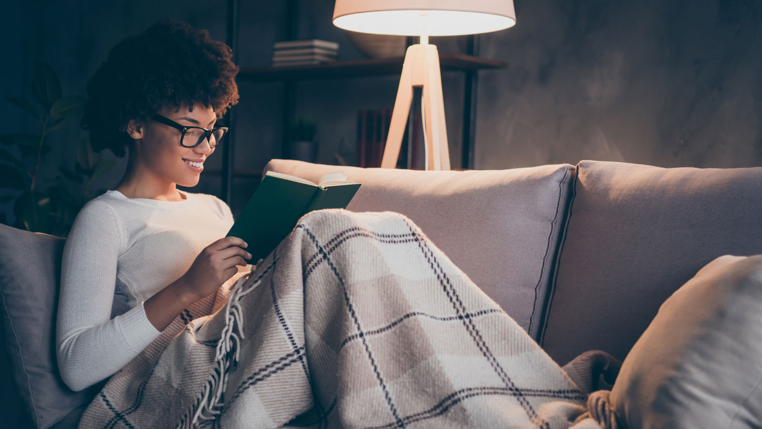 A woman covered in a blanket reading a book