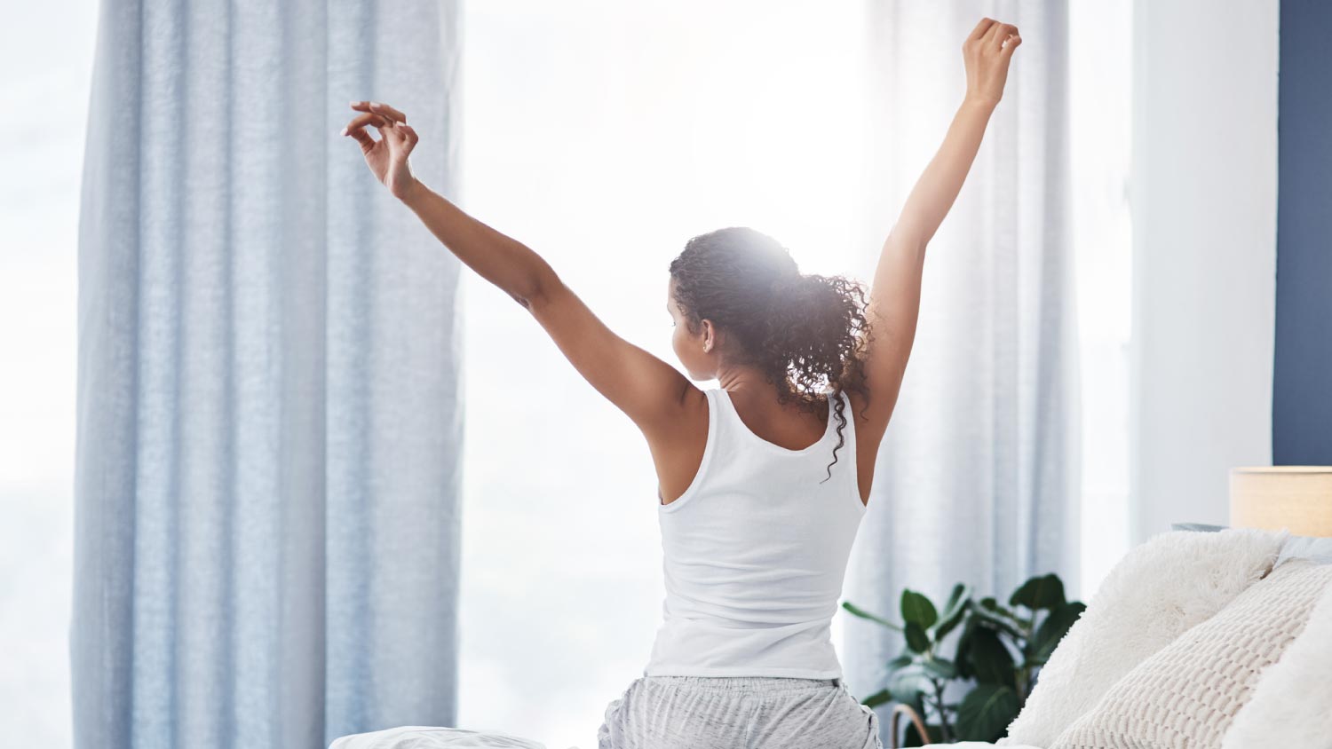 Woman stretching while sitting on her bed in the morning